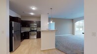 This single-floor residence offers a thoughtfully designed layout that balances open communal spaces with private retreats. The kitchen serves as a focal point, outfitted with dark espresso cabinetry, granite countertops, and a full suite of stainless steel appliances including a refrigerator, range, and over-the-range microwave. Light wood-style flooring runs throughout the kitchen and adjoining entry areas, complementing the rich cabinetry tones. A peninsula with pendant lighting above connects the kitchen to the living area, providing both additional counter space and a natural transition between the two zones.

The living area is generously proportioned and finished with neutral carpet. A graceful arched opening leads to a bright sunlit nook framed by a wide multi-pane window, flooding the space with natural light. The bedroom continues the carpeted, light-toned aesthetic, featuring a window with outdoor views and a ceiling fan fixture.

The bathrooms are well-appointed, with one featuring a soaking tub with curved surround and the other offering a dark-cabineted vanity with a large mirror and walk-in closet access. Light wood flooring ties the bathrooms together cohesively. A dedicated in-unit laundry closet near the entry provides full-size washer and dryer hookups, adding everyday convenience to this well-rounded residence.