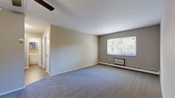 Located at 680 Smith Court in Rocky River, OH, this one-bedroom, one-bathroom unit offers a well-organized single-floor layout designed for efficient, comfortable living. The living room is the largest space in the unit, featuring plush wall-to-wall carpeting, neutral taupe-toned walls, and a ceiling fan with integrated lighting. Decorative wainscoting with paneled molding adds a classic architectural touch to the living area. A window unit air conditioner and baseboard heating ensure year-round climate control, while a window overlooking the surrounding greenery brings in natural light and pleasant outdoor views. The bedroom continues the carpeted flooring with its own baseboard heating and a window framing views of mature trees. The entrance hallway connects the main living areas via hardwood-style flooring, providing a clean transition between spaces. The bathroom features a full soaking tub and shower combination surrounded by a bold two-toned tile surround in dark brown and white, complemented by hardwood-style flooring, a white vanity with an integrated sink, and a mirrored medicine cabinet. The overall ambiance of this unit is understated and functional, with consistent neutral finishes throughout.