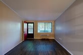 Located at 7250 Campbellton Rd SW in South Fulton, GA, this efficient single-floor unit offers a well-organized layout comprising a living room, kitchen, and full bathroom. The living area is bright and open, featuring dark hardwood-style flooring, warm neutral-toned walls, and a large window that frames views of surrounding greenery, allowing natural light to fill the space. A bold red entry door adds a distinctive touch to the interior. A wall-mounted HVAC unit provides climate control directly within the living area. The kitchen is thoughtfully designed with white cabinetry, a mosaic tile backsplash, granite-style countertops, a stainless steel sink, and a compact appliance suite. An open pass-through shelf connects the kitchen visually to the living space, enhancing the sense of openness. A closet adjacent to the kitchen area provides convenient built-in storage. The bathroom is clean and functional, finished with matching granite-style countertops, a single vanity sink, a toilet, and a bathtub, all set against warm beige walls with consistent hardwood-style flooring. The textured ceilings in portions of the space add a classic architectural detail throughout this cozy, efficiently designed unit.