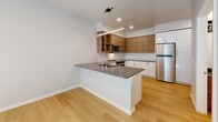This contemporary 1-bedroom apartment in Seattle offers a thoughtfully designed living space within its 570 square feet. The open-concept floor plan maximizes the use of space, creating a seamless flow between the living areas. The kitchen is a standout feature, boasting sleek white cabinetry contrasted with warm wood upper cabinets, stainless steel appliances, and a stylish island with a quartz countertop that doubles as a dining area.

The bathroom showcases a modern aesthetic with a wood vanity, white countertop, and a combination tub-shower with crisp white tiling. The bedroom, measuring 110 square feet, offers ample space and is enhanced by a large window that allows natural light to flood the room. Light wood flooring runs throughout the apartment, adding warmth and continuity to the space.

A unique sliding barn door provides privacy and adds a touch of industrial chic to the interior design. The apartment also includes a closet for storage. Recessed lighting and contemporary fixtures contribute to the overall modern ambiance. Located at 2222 15th Ave W in Seattle, this efficient single-floor dwelling combines style and functionality in a compact urban setting.