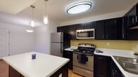 This single-story residence at 215 Codell Dr in Lexington, Kentucky offers a well-organized layout with distinct living, kitchen, bedroom, and bathroom areas. The entry opens into a combined living and dining space featuring warm wood-look flooring and a pendant light fixture, creating a welcoming first impression.

The kitchen is a standout feature, showcasing dark espresso-toned cabinetry that extends to the ceiling for generous storage, complemented by white countertops, stainless steel appliances including a range, microwave, and refrigerator, and a double basin sink. A central kitchen island with pendant lighting above provides additional workspace and casual seating potential. The wood-look flooring continues throughout this area, adding warmth and continuity.

The bedrooms are carpeted for comfort, each featuring neutral walls, blinds-covered windows that admit natural light, and ceiling-mounted light fixtures. One bedroom includes a ceiling fan. The unit includes two bathrooms: one with a walk-in shower and tile flooring, and another with a full tub-shower combination and matching tile. Both bathrooms feature dark vanity cabinetry consistent with the kitchen's design aesthetic, creating a cohesive look throughout the residence.