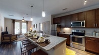 This single-floor residence offers a thoughtfully designed open-concept layout that seamlessly connects the kitchen, dining, and living areas. The kitchen is a standout feature, showcasing rich dark-wood cabinetry, granite countertops, stainless steel appliances including a refrigerator, range, and microwave, and a large central island with bar seating illuminated by elegant pendant lighting. Wood-style flooring flows throughout the main living areas, adding warmth and continuity to the space.

The living room is bright and welcoming, anchored by large French doors that flood the room with natural light and offer views of the surrounding greenery. A ceiling fan adds comfort, while the open sightlines to the kitchen create an ideal environment for entertaining.

Two well-proportioned bedrooms each feature wood-style flooring, ceiling fans, and large windows that invite natural light. The primary bedroom is complemented by an ensuite bathroom appointed with a double-sink granite vanity, a glass-enclosed shower, and large-format tile flooring. A second full bathroom mirrors the same quality finishes, featuring a granite vanity and a tub-shower combination. Together, the rooms and finishes create a cohesive, modern living experience with attention to detail throughout.