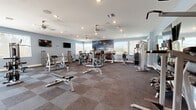 Located at 750 W Orange Grove Rd in Tucson, Arizona, this fitness center offers a generously sized, single-floor workout facility designed to support a full range of exercise routines. The space is finished with a durable two-tone carpet tile flooring and painted in a cool, calming blue-gray palette, creating an energizing yet comfortable atmosphere throughout.

Natural light fills the room through multiple large windows positioned along the perimeter walls, offering views of the surrounding Tucson landscape. Ceiling fans and recessed lighting provide additional comfort and visibility during workouts. A striking large-scale mural serves as a bold focal point on one wall, adding a dynamic visual element to the space.

The facility is comprehensively equipped with a row of TRUE brand treadmills and cardio machines, multiple selectorized strength machines, cable systems, adjustable benches, and a dedicated free weight area with a dumbbell rack and wall-mounted mirrors. Stability balls, medicine balls, and battle ropes round out the functional fitness offerings. Wall-mounted flat-screen televisions are positioned throughout for entertainment during workouts. The layout is thoughtfully organized to allow ample space between equipment, ensuring a safe and comfortable training environment for all users.