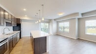Located at 240 Thompson Ave E in West St. Paul, MN, this well-appointed 2-bedroom, 2-bathroom residence offers a thoughtfully designed single-level layout. The open-concept kitchen and living area serves as the heart of the home, anchored by a large center island with a bright white countertop and stylish pendant lighting. The kitchen features rich dark cabinetry, a classic subway tile backsplash, stainless steel appliances, and recessed lighting, creating a functional yet attractive space. Light wood-style flooring flows throughout the main living areas, enhancing the bright and airy atmosphere. Sliding glass doors lead to a private balcony that overlooks lush, mature greenery and well-maintained landscaping, providing a peaceful outdoor retreat. Both bedrooms are comfortably sized and finished with plush carpeting and windows that invite natural light. The primary bedroom includes a spacious walk-in closet. The bathrooms are clean and modern, with one featuring a glass-enclosed walk-in shower with large-format white tile. Additional highlights include a hallway connecting the private quarters, three closets for generous storage, a dedicated laundry area with in-unit washer/dryer hookups, and a utility room. A bold navy entry door adds a distinctive design touch to this move-in-ready home.