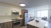 Located at 66 Summer Street in Stamford, Connecticut, this single-floor residence offers a thoughtfully designed open-concept layout that seamlessly connects the kitchen and living areas. The kitchen is outfitted with stainless steel appliances, including a GE range, over-the-range microwave, and a full-size refrigerator. Rich wood-toned cabinetry is paired with crisp white upper cabinets and light-colored countertops, creating a modern, two-tone aesthetic. A kitchen island provides additional prep and dining space, enhancing the functional flow of the room. The living area is bright and airy, benefiting from natural light streaming through large windows. The open floor plan allows the kitchen, dining, and living spaces to interact naturally, making the residence feel welcoming and spacious. Smooth white ceilings with flush-mount lighting add to the clean, contemporary finish throughout. Light hardwood-style flooring runs through the main living areas, tying the design together with warmth and cohesion. This well-appointed residence combines modern finishes with a practical layout, making it an ideal space for comfortable everyday living in the heart of Stamford.