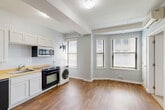 Located at 1538 Centre St in the heart of Detroit, MI, this two-bedroom, one-bathroom unit offers a thoughtfully arranged single-floor layout that maximizes every inch of its compact footprint. The open-plan living and dining area serves as the central hub of the home, bathed in natural light through multiple large windows dressed with blinds. Warm hardwood-style flooring runs throughout the main living space, lending a clean, cohesive aesthetic anchored by exposed structural beams overhead that add an industrial character to the interior. The kitchen is efficiently designed with white shaker-style cabinetry, butcher block countertops, a full suite of appliances including a refrigerator, electric range, dishwasher, and over-the-range microwave, as well as a convenient in-unit washer tucked neatly alongside. Both bedrooms feature plush carpeting, natural light from windows, and a calm, neutral color palette in soft grey tones. The primary bedroom offers a generous layout with ample room for furnishings. The full bathroom is finished with white tile flooring and includes an accessible tub/shower combination equipped with grab bars. A dedicated utility room rounds out the functional amenities of this well-organized urban residence.