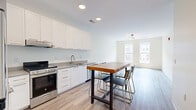 Located at 87 Union St in New Haven, CT, this thoughtfully designed one-bedroom, one-bathroom unit offers a clean, modern aesthetic across a single floor. Light-toned hardwood flooring flows throughout, contributing to an airy and cohesive feel.

The open kitchen and living area forms the heart of the unit. The kitchen is well-appointed with white flat-front cabinetry, gray countertops, stainless steel appliances including a full-size refrigerator, electric range, dishwasher, and a natural live-edge wood island with seating — a standout design feature that adds warmth and character to the space.

The bedroom is comfortably sized with large windows that allow natural light to fill the room and offer views of the surrounding neighborhood. A modern globe-cluster light fixture adds a stylish touch to the otherwise clean and minimal design.

The bathroom is finished to a high standard, featuring large-format gray tile surrounding a soaking tub with shower, matte black fixtures throughout, a white vanity with gray countertop, and an oversized mirror with integrated lighting — delivering a contemporary, spa-like feel.

A connecting hallway provides practical separation between rooms. Throughout the unit, the design prioritizes clean lines, neutral tones, and quality finishes, creating a bright and functional living space in the heart of New Haven.