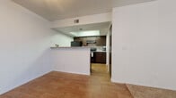 This single-floor residence offers a thoughtfully designed layout that balances functionality and comfort across its key living areas. The kitchen is equipped with dark espresso cabinetry, black appliances including a refrigerator and electric range, and a mosaic tile backsplash that adds visual interest. A half-wall peninsula separates the kitchen from the adjacent living space, creating an open, connected feel while maintaining defined zones. Wood-look flooring flows throughout the kitchen and entryway areas, providing a warm and durable foundation. The living room is generously sized, featuring plush neutral carpeting, a ceiling fan with integrated lighting, and sliding glass doors fitted with vertical blinds that allow for natural light and outdoor access. A fireplace with a classic surround and arched wall niches serve as charming architectural accents, lending character to the main living space. A separate bedroom offers its own sliding glass door access, continuing the carpet and vertical blind design for a cohesive look. The full bathroom includes a single-sink vanity with dark wood cabinetry, a tub and shower combination, and hardwood-style flooring. A dedicated in-unit laundry room houses a full-size washer and dryer side by side, adding significant convenience to daily living.