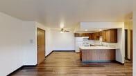 This single-floor unit offers a practical and well-organized layout designed for comfortable everyday living. The open-concept kitchen is a central feature, equipped with warm oak cabinetry, light-toned countertops, a double sink, and white appliances including a refrigerator and range. A peninsula island extends into the living area, creating a natural transition between the kitchen and the main living space. The living area combines durable wood-style vinyl flooring near the kitchen with plush carpeting in the lounge zone, and benefits from a large window that invites natural light and outdoor views. A wall-mounted HVAC unit provides additional climate control. The bedrooms are spacious and carpeted, each featuring baseboard heating and generously sized windows that frame views of the surrounding greenery, creating a calm and airy atmosphere. The bathroom is cleanly appointed with tile flooring, a wood-toned vanity with a light countertop, a large mirror, and a tub and shower combination with a sliding glass door. Throughout the unit, consistent use of warm wood tones, neutral wall colors, and practical finishes creates a cohesive and livable environment. Baseboard heating runs throughout, ensuring comfort across the seasons.