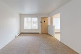 This single-floor unit in Royal Oak, Michigan, offers a straightforward, functional layout with clearly defined living zones. The floor plan, visible in the dollhouse view, reveals an efficient arrangement of interconnected rooms with neutral white walls throughout, creating a clean, blank-canvas atmosphere well-suited for customization.

The living area is generously proportioned, featuring wall-to-wall beige carpeting and bright white walls. Large windows fitted with vertical blinds admit ample natural light, while baseboard heating runs along the perimeter walls. An open entryway connects this space directly to adjacent rooms, facilitating easy flow throughout the unit.

The galley-style kitchen is lined on both sides with dark brown cabinetry, offering considerable storage capacity both above and below the white laminate countertops. A double sink, a full-size white refrigerator, and additional appliances are included. Light-toned vinyl flooring completes the kitchen.

Bedrooms continue the carpeted theme and maintain the neutral palette. At least one bedroom includes a built-in closet with bifold doors, a shelving unit, and a window with vertical blinds that provides outdoor views and natural light. Baseboard heaters are present in these rooms as well.

The bathroom features a full-size white soaking tub with chrome fixtures, surrounded by classic white square ceramic tile walls, offering a clean, utilitarian finish.