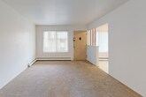 This single-floor unit in Royal Oak, Michigan, offers a straightforward, functional layout with clearly defined living zones. The floor plan, visible in the dollhouse view, reveals an efficient arrangement of interconnected rooms with neutral white walls throughout, creating a clean, blank-canvas atmosphere well-suited for customization.

The living area is generously proportioned, featuring wall-to-wall beige carpeting and bright white walls. Large windows fitted with vertical blinds admit ample natural light, while baseboard heating runs along the perimeter walls. An open entryway connects this space directly to adjacent rooms, facilitating easy flow throughout the unit.

The galley-style kitchen is lined on both sides with dark brown cabinetry, offering considerable storage capacity both above and below the white laminate countertops. A double sink, a full-size white refrigerator, and additional appliances are included. Light-toned vinyl flooring completes the kitchen.

Bedrooms continue the carpeted theme and maintain the neutral palette. At least one bedroom includes a built-in closet with bifold doors, a shelving unit, and a window with vertical blinds that provides outdoor views and natural light. Baseboard heaters are present in these rooms as well.

The bathroom features a full-size white soaking tub with chrome fixtures, surrounded by classic white square ceramic tile walls, offering a clean, utilitarian finish.