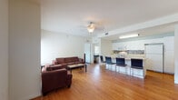 This single-floor unit offers a well-organized layout designed for comfortable, functional living. The open-concept living and dining area is anchored by warm hardwood-style flooring and a ceiling fan, creating a bright and airy atmosphere. A large window floods the living space with natural light and provides views of the tree-lined surroundings. The kitchen flows seamlessly from the living area and features white cabinetry, a decorative mosaic tile backsplash, light countertops, and a breakfast bar with seating — ideal for casual dining. White appliances, including an electric range and over-the-range microwave, complete the kitchen's practical setup. Multiple bedrooms share a consistent design, each featuring hardwood-style flooring, a window for natural light, a built-in desk workspace, and an open shelving closet — making them well-suited for study and rest. The unit includes several full bathrooms, each finished with light tile flooring, white vanity cabinetry, a large mirror, and a full tub and shower combination with white tile surround. Clean, neutral tones throughout the unit create a cohesive and low-maintenance aesthetic, while the efficient single-floor layout ensures easy accessibility across all spaces.