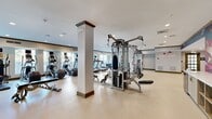 Located at 1020 Lenox Park Blvd NE in Atlanta's Lenox Park neighborhood, this generously sized fitness center spans a single floor and offers a comprehensive, well-equipped workout facility. The space is organized into distinct functional zones, each designed to support a variety of training needs.

The main exercise floor is bright and open, with large windows along one wall that flood the area with natural light and offer outdoor views. This section houses a robust selection of cardio equipment, including treadmills, elliptical machines, and stationary bikes with integrated screens, alongside a full multi-station Hoist cable machine and a rack of dumbbells for strength training. Floor-to-ceiling mirrors line portions of the walls, enhancing the sense of space.

A dedicated studio area features stylish drum pendant lighting and open floor space, supported by wall-mounted mirrors and equipment racks stocked with medicine balls, suspension trainers, and accessories — ideal for functional fitness and group training sessions. A vibrant large-scale floral mural adds an artistic focal point to one wall, creating an energizing atmosphere.

Additional highlights include a Peloton cycling alcove with a wall-mounted water fountain, recessed and accent lighting throughout, light-toned resilient flooring, and motivational neon signage reading "Don't Quit." The overall design balances functionality with modern aesthetic appeal.