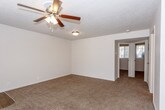 This single-story residence offers a thoughtfully arranged layout that balances open communal spaces with private quarters. The living area is generously proportioned, featuring plush wall-to-wall carpeting, neutral-toned walls, a textured ceiling, and a ceiling fan with integrated lighting. A large window fitted with horizontal blinds allows natural light to fill the space, while a nearby entry door provides direct access. The living area connects seamlessly to the kitchen, creating an open, functional flow.

The kitchen is a standout feature, showcasing dark espresso-toned cabinetry that extends to the upper and lower walls, paired with light quartz countertops and a central island that adds additional workspace and storage. Stainless steel appliances, including a dishwasher and refrigerator, complement the wood-look vinyl flooring and a window that brings in natural light.

The bedrooms continue the carpeted flooring theme, each equipped with ceiling fans, ample wall space, and windows with blinds for natural light and privacy. The bathroom is finished with dark wood cabinetry, a white countertop vanity, wood-look tile flooring, and a full tub-shower combination, maintaining a cohesive and clean aesthetic throughout the home.