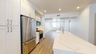 Located at 6720 Calle Koral in Goleta, California, this single-story residence offers a clean, contemporary design with a bright and airy aesthetic throughout. The open-concept layout connects the kitchen and living area seamlessly, creating a spacious and functional flow. The kitchen is a standout feature, showcasing a large center island topped with elegant veined quartz countertops, white shaker-style cabinetry with brushed gold hardware, and a full suite of stainless steel appliances including a gas range, microwave, and a full-size refrigerator. Light wood-look flooring runs throughout the main living areas, complementing the crisp white walls and recessed lighting. The living area is generously proportioned, with a ceiling fan, natural light from large windows fitted with blinds, and access to an exterior door. The bedrooms are carpeted for comfort, each featuring ceiling fans, bright windows with outdoor views, and a clean, neutral palette. The primary bathroom is appointed with a double-sink quartz vanity, white cabinetry, brushed nickel fixtures, and a well-lit mirror. A secondary bathroom provides additional convenience with a matching design aesthetic. Throughout, the home maintains a consistently modern, move-in-ready character with thoughtful finishes and an abundance of natural light.