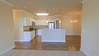 Located at 1850 Popps Ferry Rd in Biloxi, Mississippi, this single-story home offers a well-designed open-concept layout that seamlessly connects the kitchen and living areas. The kitchen is a standout feature, showcasing white raised-panel cabinetry, granite countertops, and a full suite of stainless steel appliances, including a range, microwave, and refrigerator. A large central island provides additional counter space and serves as a natural gathering point. Pendant lighting above the island and an elegant chandelier in the adjoining dining area add warmth and character to the space. Crown molding runs throughout, lending a refined, polished look to every room. The flooring transitions from rich hardwood-style planks in the main living and kitchen areas to plush carpet, offering both durability and comfort underfoot. Warm, neutral wall tones create a bright and inviting atmosphere that complements the natural light flowing through the space. The open flow between the kitchen, dining, and living areas makes this home feel spacious and functional, ideal for both everyday living and entertaining.