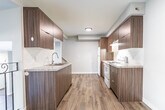 This two-storey home in Hamilton's East Mountain neighbourhood offers 3 bedrooms and 2 bathrooms across two well-proportioned floors. The main level features a bright living room with large windows overlooking a private fenced patio, allowing generous natural light and outdoor views. The galley-style kitchen is a standout, showcasing rich walnut-toned cabinetry extending floor to ceiling, light granite-style countertops, a subway tile backsplash, a stainless steel sink, and white appliances including a refrigerator and electric range. Light wood-look laminate flooring flows consistently throughout both levels, creating a cohesive and modern aesthetic. A staircase with a sleek black metal railing connects the floors. The upper level hosts three bedrooms, each finished with neutral tones, laminate flooring, and closets — including mirrored sliding closet doors in select rooms. The primary bedroom features a wide window with neighbourhood views. Two bathrooms serve the home with clean, functional layouts. Neutral grey-white walls throughout contribute to a fresh, move-in-ready feel. The space is efficiently laid out across both floors, making practical use of every area while maintaining a clean, contemporary look.