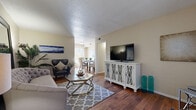 This single-story residence is finished with warm hardwood flooring that flows consistently throughout, creating a cohesive and inviting atmosphere across all rooms. The living area is generously proportioned, offering space for both a seating arrangement and a dedicated sitting nook. A textured ceiling adds visual interest overhead, while neutral walls provide a versatile backdrop. The living space opens toward the dining area, which benefits from a large sliding glass door fitted with vertical blinds, drawing in natural light and providing access to an outdoor patio.

The galley-style kitchen features dark espresso cabinetry paired with light countertops, a stainless steel sink, and black appliances including a refrigerator, range, and dishwasher. A secondary door at the end of the kitchen offers additional exterior access.

The bedroom is a well-sized retreat with a ceiling fan, a window with natural light, and two separate closet doors offering ample storage. The bathroom is elongated and functional, presenting an extended vanity with dark cabinetry, dual mirrors, and a separate water closet, delivering both practicality and a refined finish throughout.