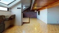 This distinctive two-story, 2-bedroom, 1.5-bathroom home is defined by its striking architectural character and industrial-meets-rustic aesthetic. The main living area immediately impresses with its expansive exposed brick walls, warm wood-planked ceiling supported by substantial timber beams, and parquet wood flooring laid in a classic checkerboard pattern. A built-in raised platform adds dimension and visual interest to the space, while skylights and clerestory windows bathe the room in natural light. Exposed black piping runs along the upper walls, reinforcing the loft-inspired industrial charm. A chandelier adds a touch of warmth overhead.

The kitchen is functional and well-equipped, featuring dark wood cabinetry, tile backsplash with decorative accent tiles, and ample counter space alongside a full suite of appliances.

The bedrooms continue the home's signature aesthetic with exposed brick accent walls, skylights, and carpeted floors, offering a cozy contrast to the open living areas. Sloped ceilings lend each room an intimate, attic-like quality.

The full bathroom is clean and bright, outfitted with a tub-shower combination, white tile surround, mosaic tile flooring, and a white vanity with storage. The overall ambiance of this home is warm, textural, and full of architectural personality.