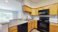 Located at 51 Great Trail Cir in Pickerington, Ohio, this two-story residence offers a practical and comfortable layout across both levels. The kitchen is well-appointed with warm oak cabinetry providing generous storage, light-toned countertops, and a full suite of black appliances including a refrigerator, electric range, over-the-range microwave, and dishwasher. A pass-through counter connects the kitchen to the adjacent living area, enhancing the open feel between spaces. The living room is generously sized, finished with plush carpet and neutral-toned walls, and features a large sliding glass door framed by vertical blinds that floods the room with natural light and provides access to the outdoors. The bedrooms are carpeted and bright, each benefiting from windows that offer views of the surrounding greenery. Warm wood-toned doors and trim carry throughout the home, lending a cohesive and inviting character. The bathroom includes an oak vanity with a white countertop and sink, a tub-shower combination, and durable wood-look flooring. Textured ceilings and recessed lighting are found throughout, contributing to the home's understated, functional aesthetic. The staircase connecting the two floors is visible from the main living area, reinforcing the home's multi-level design.