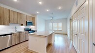 This thoughtfully laid-out 1-bedroom, 1-bathroom residence offers a clean, modern aesthetic throughout its single floor. The open-concept kitchen and living area serves as the heart of the space, anchored by a central island with granite countertops that provides both workspace and casual seating. The kitchen is fully equipped with stainless steel appliances — including a refrigerator with ice maker, electric range, microwave, and dishwasher — complemented by warm wood-toned cabinetry, a subway tile backsplash, and light hardwood-style flooring. A built-in beverage cooler beneath the island adds a refined touch. The living area extends naturally from the kitchen, brightened by a bank of windows with blinds and a ceiling fan overhead. The bedroom offers plush carpeting, natural light from multiple windows, a ceiling fan, and a sliding barn-style closet door for added character. The bathroom features a granite-topped vanity with wood cabinetry, a tub/shower combination, and matching hardwood-style flooring that carries a cohesive design throughout. Recessed lighting and clean white walls create a bright, contemporary ambiance across the entire residence.