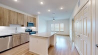 This thoughtfully laid-out 1-bedroom, 1-bathroom residence offers a clean, modern aesthetic throughout its single floor. The open-concept kitchen and living area serves as the heart of the space, anchored by a central island with granite countertops that provides both workspace and casual seating. The kitchen is fully equipped with stainless steel appliances — including a refrigerator with ice maker, electric range, microwave, and dishwasher — complemented by warm wood-toned cabinetry, a subway tile backsplash, and light hardwood-style flooring. A built-in beverage cooler beneath the island adds a refined touch. The living area extends naturally from the kitchen, brightened by a bank of windows with blinds and a ceiling fan overhead. The bedroom offers plush carpeting, natural light from multiple windows, a ceiling fan, and a sliding barn-style closet door for added character. The bathroom features a granite-topped vanity with wood cabinetry, a tub/shower combination, and matching hardwood-style flooring that carries a cohesive design throughout. Recessed lighting and clean white walls create a bright, contemporary ambiance across the entire residence.