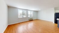 Located at 9503 State Rd in Philadelphia's 19114 neighborhood, this 2-bedroom, 2-bathroom residence offers a thoughtfully designed single-floor layout with a clean, modern aesthetic throughout. The spacious living room is bathed in natural light from a pair of large windows with blinds and features warm hardwood-style flooring, a wall-mounted HVAC unit, and a distinctive arched architectural detail that adds a touch of character to the space. The kitchen is a standout feature, showcasing two-tone cabinetry with white upper cabinets and gray lower cabinets, white subway tile backsplash, light countertops, and black appliances including a range, built-in microwave, and dishwasher. A kitchen island provides additional workspace and storage. Both bedrooms are generously proportioned, carpeted for comfort, and include windows that let in natural light. The primary bedroom offers ample space and closet access. The two bathrooms are finished with neutral tile flooring, dark vanity cabinetry, light countertops, and modern fixtures; one features a full tub-shower combination. Three hallways connect the rooms efficiently, and a dedicated closet adds practical storage. The overall palette of soft grays, whites, and warm wood tones creates a bright, neutral ambiance throughout.