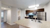 Located at 4155 Satellite Blvd in Duluth, GA, this single-floor unit offers a well-designed layout with a blend of practical finishes and comfortable living spaces throughout. The spacious living room is a standout feature, showcasing rich dark hardwood-style flooring, a ceiling fan, and a large bay window arrangement that floods the room with natural light while offering views of the surrounding greenery. A door provides convenient exterior access directly from this area. Adjacent to the living room, the dining area flows seamlessly toward the kitchen, which is appointed with dark espresso cabinetry, light granite-style countertops, a subway tile backsplash in a soft blue-gray tone, and stainless steel appliances including a range and refrigerator. A peninsula with a built-in sink adds additional prep and seating space. An in-unit laundry area is conveniently accessible from the kitchen. The bedrooms are generously sized, featuring plush carpeting, natural window light, and well-sized closets. The bathroom is clean and functional, featuring a tub-shower combination with white tile surround, dark wood vanity, and hardwood-style flooring. Textured ceilings are consistent throughout the unit, contributing to its classic residential character.