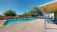 Located on Cristo Viene Dr in El Paso, TX, this two-level property features a well-appointed outdoor recreational area designed to make the most of the sunny Chihuahuan Desert climate. The centerpiece of the outdoor space is a generously sized rectangular swimming pool with clear turquoise water, flanked by a wide concrete pool deck lined with multiple lounge chairs for sunbathing. Adjacent to the main pool is a smaller, circular wading pool, ideal for younger guests or those seeking a more relaxed water experience. The pool area is enclosed by a distinctive rustic stone wall along one side, complemented by metal security fencing that defines the perimeter while allowing views of the surrounding mature trees, which provide natural shade and greenery. A covered facility building sits alongside the pool deck, offering a shaded retreat and housing pool-related amenities and posted pool rules. The broad concrete surround provides ample space for lounging and movement throughout the area. Mature trees dotting the landscape offer a natural canopy, softening the hardscape and adding a welcoming, park-like ambiance to the overall setting beneath El Paso's characteristically bright blue skies.