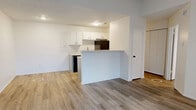 This 1-bedroom, 1-bathroom unit offers a thoughtfully organized single-floor layout with a clean, modern aesthetic throughout. Light wood-look laminate flooring runs consistently across all rooms, complementing the bright white walls and textured ceilings that characterize the space.

The combined kitchen and living area forms the heart of the unit. The kitchen features a galley-style configuration with gray lower cabinets, white upper cabinets, light quartz-style countertops, a black sink with a matte black faucet, and black appliances including a refrigerator, electric range, and dishwasher. A peninsula with a raised counter neatly separates the kitchen from the open living area, which benefits from a front-facing window that allows natural light to filter in.

The bedroom is a well-proportioned, private retreat fitted with a ceiling fan, two windows that brighten the room naturally, and direct access to a dedicated closet with built-in shelving rods on multiple walls, offering generous storage capacity.

The bathroom is finished with a gray vanity, quartz-style countertop, a large mirror, matte black fixtures, and a clean, bright overall presentation. Throughout the unit, clean lines, neutral tones, and consistent finishes create a cohesive and practical living environment.