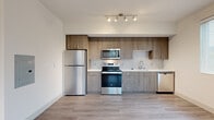 Located at Bear Creek Parkway in Redmond, Washington, this single-floor residence presents a thoughtfully designed interior with a cohesive modern aesthetic throughout. The kitchen serves as a standout feature, showcasing floor-to-ceiling wood-tone cabinetry with brushed nickel hardware, a textured tile backsplash, and a full suite of stainless steel appliances including a refrigerator, electric range, over-the-range microwave, and dishwasher. White quartz-style countertops complement the warm cabinetry tones, while wood-look tile flooring extends across the open living and kitchen area, adding warmth and continuity. Recessed track lighting overhead ensures the kitchen is well-illuminated. The bedroom offers plush carpeting, a ceiling fan, a generously sized closet with built-in shelving, and a window that allows natural light to filter in. The bathroom features marble-look porcelain tile flooring, a wood-tone vanity with an undermount sink, a framed mirror with a multi-bulb vanity light fixture above, and a clean, bright ambiance. The overall layout, as seen in the 3D overview, provides a functional and open flow between the living, kitchen, and private spaces.