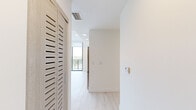 Located at 1601 SW 32nd Ave in Miami, FL, this modern unit offers five bedrooms and two full bathrooms across a thoughtfully designed single-floor layout. The interior is defined by light-toned luxury vinyl plank flooring, crisp white walls, and recessed lighting that create a bright, clean aesthetic throughout.

The living area is a true standout, featuring a dramatic curved wall of floor-to-ceiling glass panels with sleek black frames that open to a private balcony. This sweeping glass facade floods the space with natural light and provides panoramic views of the surrounding Miami greenery and skyline.

The kitchen is equipped with stainless steel appliances — including a refrigerator, range, microwave, and dishwasher — complemented by light wood cabinetry and a clean countertop that seamlessly integrates with the open-plan living area.

Each of the five bedrooms is finished in the same bright, minimalist palette, with large black-framed windows inviting natural light and outdoor views. Select bedrooms feature built-in closets with multi-tier shelving for organized storage. A central hallway connects all rooms efficiently.

Both bathrooms are identically appointed with wood-toned vanities, integrated sinks, and full soaking tubs with shower combinations, maintaining a cohesive and functional design. The overall ambiance is modern, airy, and well-suited for comfortable multi-occupant living.