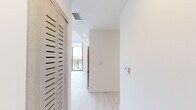 Located at 1601 SW 32nd Ave in Miami, FL, this modern unit offers five bedrooms and two full bathrooms across a thoughtfully designed single-floor layout. The interior is defined by light-toned luxury vinyl plank flooring, crisp white walls, and recessed lighting that create a bright, clean aesthetic throughout.

The living area is a true standout, featuring a dramatic curved wall of floor-to-ceiling glass panels with sleek black frames that open to a private balcony. This sweeping glass facade floods the space with natural light and provides panoramic views of the surrounding Miami greenery and skyline.

The kitchen is equipped with stainless steel appliances — including a refrigerator, range, microwave, and dishwasher — complemented by light wood cabinetry and a clean countertop that seamlessly integrates with the open-plan living area.

Each of the five bedrooms is finished in the same bright, minimalist palette, with large black-framed windows inviting natural light and outdoor views. Select bedrooms feature built-in closets with multi-tier shelving for organized storage. A central hallway connects all rooms efficiently.

Both bathrooms are identically appointed with wood-toned vanities, integrated sinks, and full soaking tubs with shower combinations, maintaining a cohesive and functional design. The overall ambiance is modern, airy, and well-suited for comfortable multi-occupant living.