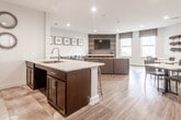 Located at 1420 Campbell St in Rahway, New Jersey, this single-floor community amenity space is designed with a contemporary aesthetic and a functional, open-plan layout. The space features warm wood-look flooring throughout, recessed lighting, and crisp white walls that create a bright and welcoming atmosphere.

The main lounge area serves as the focal point, anchored by a striking media wall clad in geometric patterned tile with wood framing, housing a large flat-screen TV and built-in shelving. A pair of upholstered ottomans and a sectional sofa provide comfortable seating, while multiple windows dressed with roman shades allow natural light to fill the room.

Adjacent to the lounge, a kitchenette features a countertop bar with wire-frame bar stools, an under-mount sink, open wood shelving, and decorative accents — ideal for casual gatherings. French doors connect this area to the broader space, enhancing flow and accessibility.

A dedicated work and dining zone includes small white-top tables paired with sleek blue-grey chairs, as well as a long wall-mounted countertop lined with bar-height seating beneath a series of framed black-and-white artwork. A wall-mounted wine or bottle rack adds a stylish touch to this area. A restroom is conveniently accessible from the lounge corridor. Overall, the space balances social interaction with productivity in a polished, modern setting.