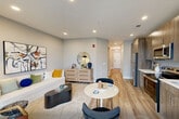 Located at 155 Goldsborough Dr in Bayonne, NJ, this one-bedroom, one-bathroom residence offers a thoughtfully designed single-floor layout that maximizes every inch of its compact footprint. Light wood-tone flooring flows consistently throughout, creating a cohesive and airy atmosphere.

The kitchen is a standout feature, outfitted with wood-grain cabinetry extending from floor to ceiling, crisp white quartz countertops, a neutral tile backsplash, and a full suite of stainless steel appliances including a refrigerator, range, microwave, and dishwasher. The space is both functional and visually polished.

The living area is bright and open, with recessed lighting, soft gray walls, and enough room to accommodate a comfortable seating arrangement. A short hallway connects the main living space to the private bedroom, which features the same warm flooring and neutral tones. The bedroom is cozy and well-proportioned, with recessed lighting and clean wall surfaces that provide a calm, restful environment.

The bathroom is finished with a combination of wood-look and light gray subway tiles surrounding a soaking tub with an overhead rain showerhead and chrome fixtures. The light-toned flooring continues here, tying the design together throughout the unit.