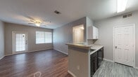 Located at 10127 State Highway 16 S in San Antonio, TX, this single-floor unit offers a thoughtfully designed layout with modern finishes throughout. The open-concept living and kitchen area serves as the heart of the space, where wood-style flooring, neutral gray walls, and ceiling fans create a clean, comfortable atmosphere. Natural light flows in through windows fitted with blinds, brightening the living area, which also features a glass-panel front door for added brightness.

The kitchen is equipped with dark lower cabinetry contrasted by white upper cabinets, granite-style countertops, a peninsula with a built-in sink, and black appliances including a full-size refrigerator. A separate galley-style kitchen corridor provides ample workspace and storage.

The bedrooms are generously sized, each featuring wood-style flooring, ceiling fans, and windows that invite natural light. The hallway connects the living spaces to the private areas of the unit seamlessly.

The bathroom includes a tiled tub-shower combination with a classic white and terracotta accent tile design, while a second bathroom offers a vanity with dark cabinetry, a mirror, and a medicine cabinet. Wood-style flooring carries throughout, tying the entire space together with a cohesive, contemporary aesthetic.