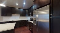 Located at 14-20 E Hubbard Ave in Columbus, Ohio, this single-floor residence offers a well-appointed layout with a cohesive design throughout. The kitchen is a standout feature, showcasing espresso-toned cabinetry that extends to the ceiling, light granite countertops, a white subway tile backsplash, and a full suite of stainless steel Whirlpool appliances including a refrigerator with ice and water dispenser, electric range, over-the-range microwave, and dishwasher. A kitchen island provides additional prep and seating space, while rich hardwood flooring anchors the kitchen and open living area. The living space is generously sized, with crown molding, recessed lighting, and large windows fitted with blinds that invite natural light. The bedroom features plush carpeting and its own set of windows with urban views. Two bathrooms serve the unit — one full bath with a quartz-topped vanity, dark cabinetry, and a walk-in shower, and one half bath with a pedestal sink and hardwood flooring. A dedicated laundry room with side-by-side washer and dryer, wire shelving, and additional cabinetry adds everyday convenience. The overall palette of warm neutrals and dark finishes creates a polished, modern ambiance.