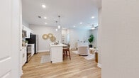 This single-story, 2-bedroom, 2-bathroom home offers a thoughtfully designed layout with a cohesive neutral palette and light wood-look flooring that flows seamlessly throughout. The open-concept kitchen and living area serves as the heart of the home, where a well-equipped kitchen features white shaker cabinetry, a classic subway tile backsplash, stainless steel appliances, white quartz countertops, and a central island with seating for three — illuminated by elegant pendant lights. The kitchen opens directly into the living area, which benefits from natural light, a ceiling fan, and access to an exterior door. A dedicated hallway connects to the bedrooms and includes a convenient in-unit laundry area. The primary bedroom is a comfortable retreat with dual windows, a ceiling fan, and its own closet. The primary bathroom offers both a soaking tub and a separate shower/tub combo, with wood-look flooring and direct closet access. The second bedroom is equally well-sized, featuring warm tones and natural light. Two hallways provide organized circulation throughout the unit, and two closets offer ample storage. The overall design maintains a clean, modern aesthetic with a warm, inviting ambiance throughout.