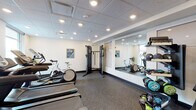 Located at 1609 SW Chandler Ave in Bend, Oregon, this dedicated fitness facility offers a comprehensive and thoughtfully organized workout environment across a single floor. The space features a drop-panel ceiling with recessed lighting that provides consistent, bright illumination throughout the room, complemented by a clean, neutral color palette of white walls and dark speckled rubber flooring designed for durability and safety.

The cardio section is well-stocked with multiple treadmills, stationary bikes, and an elliptical trainer, giving users a range of aerobic options. A large wall-mounted mirror spans one side of the room, enhancing the sense of space and allowing users to monitor their form during workouts. A cable resistance machine serves as the centerpiece for functional strength training.

The free weights area includes a multi-tier dumbbell rack with a varied selection of weights, a kettlebell stand, medicine balls, and foam rollers, catering to diverse training styles. Fitness mats and step platforms are available for floor exercises and group-style workouts. A wall-mounted water fountain station provides convenient hydration, and a waste receptacle is accessible nearby.

Framed artwork depicting Pacific Northwest landscapes adds a subtle local character to the space. The facility is clean, organized, and functional, making it a practical and well-rounded fitness destination in Bend, OR.