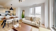 Located at 1133 Avenue Viger Est in Montréal's dynamic Ville-Marie district, this well-appointed 4-bedroom, 2-bathroom unit offers a thoughtfully designed single-floor layout. Light oak hardwood flooring flows throughout, complementing a clean, neutral palette of white walls and modern trim. The bright living room is anchored by expansive floor-to-ceiling windows that frame impressive city and bridge views, allowing natural light to fill the space. An adjacent dining area connects seamlessly to the kitchen, creating an open and functional living zone. The primary bedroom features large sliding glass doors opening to a private balcony with panoramic urban views, while additional bedrooms offer comfortable proportions, generous closet space with sliding panel doors, and access to natural light. The two bathrooms are finished in crisp white tile with matte black fixtures — one includes a soaking tub with a glass panel enclosure, while the second features a sleek frameless sliding glass shower. A welcoming hallway with panel-style interior doors and recessed lighting completes the layout. The unit's modern construction, refined finishes, and striking city views make it a standout residence in the heart of Montréal.