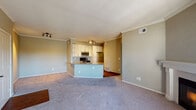 This single-floor residence is designed with an open-concept layout that seamlessly connects the living area and kitchen. The spacious living room features plush wall-to-wall carpeting, crown molding, and track lighting, creating a bright and functional space. The kitchen is well-appointed with white cabinetry, granite countertops, a light blue subway tile backsplash, and stainless steel appliances including a refrigerator, electric range, and over-the-range microwave. A peninsula with a granite countertop provides a convenient breakfast bar while defining the boundary between the kitchen and living area. The hardwood flooring in the kitchen transitions to carpet in the adjacent rooms. The bedrooms are carpeted and generously sized, with one featuring a large multi-pane window that admits abundant natural light and exterior views. The bathroom includes white cabinetry with granite countertops, a tiled tub-shower combination, and hardwood flooring. A dedicated laundry area accommodates a full-sized washer and dryer with wire shelving above for additional storage. Neutral warm-toned walls throughout contribute to a cohesive and welcoming atmosphere.