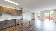 Located at 100 Commons Park North in Stamford, Connecticut, this single-floor unit offers a thoughtfully designed open-concept layout finished with rich, reclaimed hardwood-style flooring throughout. The kitchen is a standout feature, appointed with wood-grain cabinetry extending to the ceiling, crisp white countertops, a stainless steel sink, and a full suite of stainless steel appliances including a refrigerator, gas range, microwave, and dishwasher. A stainless steel island provides additional workspace and a functional focal point within the kitchen area. The living area is generous and light-filled, benefiting from expansive floor-to-ceiling windows and a sliding glass door that frames outdoor views of an adjacent terrace and brick architectural elements, allowing abundant natural light to permeate the space. The bedroom is a well-proportioned, private retreat with its own door and continued hardwood-style flooring, serviced by a dedicated HVAC vent. The bathroom features a full soaking tub and shower combo with clean white subway tile surround and contemporary chrome fixtures. The overall design aesthetic is modern and clean, with neutral walls, recessed and overhead lighting, and a cohesive material palette that lends the space a polished, contemporary feel.