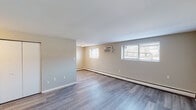 Located at 100 Christian St in Morton, Pennsylvania, this single-floor unit offers a well-maintained and updated living environment. The layout includes a spacious main living area finished with light gray wood-look vinyl plank flooring that runs throughout, neutral-toned walls, and clean white baseboards that lend a fresh, cohesive feel to the space. Multiple windows allow natural light to filter in, complemented by a wall-mounted air conditioning unit and baseboard heating for year-round comfort. The kitchen is a standout feature, showcasing gray shaker-style cabinetry, granite-look countertops, and a mosaic tile backsplash in soft blue and gray tones. It is equipped with a gas range, refrigerator, and a single-basin sink with a modern faucet, providing a fully functional cooking space. Additional rooms offer generous proportions with the same consistent flooring and neutral color palette, making them versatile for various uses. The bathroom is finished in white tile, featuring a tub-shower combination, a vanity with an integrated sink, and a mirrored medicine cabinet above, with a window providing natural ventilation. Overall, the space presents a clean, updated aesthetic with practical finishes throughout.