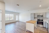This single-story, one-bedroom, one-bathroom unit offers a clean, modern aesthetic defined by crisp white walls, consistent trim work, and a neutral color palette throughout. The open-concept kitchen and living area forms the heart of the unit, where wood-look plank flooring extends across the shared space, enhancing the sense of openness. Large windows allow natural light to filter in, brightening the living area considerably.

The kitchen is well-appointed with gray shaker-style cabinetry, a white subway tile backsplash, light-toned countertops, and a full suite of stainless steel appliances, including a refrigerator, range, microwave, and dishwasher. A movable island with a butcher block top provides additional prep and storage space.

The bedroom features plush carpeting, two windows for natural light, and a ceiling fan. It connects to a dedicated walk-in closet outfitted with wire shelving and hanging rods, offering practical storage capacity.

The bathroom includes a combined tub and shower unit, wood-look vinyl flooring, and a vanity with a marble-patterned countertop. The unit's consistent, contemporary finishes throughout create a cohesive and functional living environment.