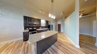 Located at 805 S 8th St in Waco, Texas, this single-floor unit combines modern finishes with an open, airy layout. The space is anchored by a striking kitchen that showcases dark espresso cabinetry, polished granite countertops, a decorative mosaic tile backsplash, and a full suite of stainless steel appliances including a range, microwave, dishwasher, and refrigerator. A large central island with pendant lighting overhead provides additional prep space and serves as a natural gathering point. Light hardwood flooring runs throughout the entire unit, complementing the soaring ceilings that lend an open, loft-like atmosphere. Track lighting is installed throughout, ensuring flexible and functional illumination in every area. The bedroom features a spacious closet and continues the consistent hardwood flooring. Large windows admit generous natural light, offering views of the surrounding greenery. The bathroom is finished with matching dark cabinetry and granite counters, maintaining the design cohesion found throughout the unit. A stacked in-unit washer and dryer add a layer of convenience. Overall, the space delivers a refined yet practical living environment with thoughtful, high-quality finishes at every turn.