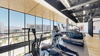 Located in Lehi, Utah, the Upper Fitness Center is a thoughtfully designed exercise facility that combines functionality with contemporary aesthetics. The single-floor space offers a generous and open layout, providing ample room for a comprehensive workout experience.

Floor-to-ceiling windows line the perimeter of the cardio area, flooding the space with natural light and offering sweeping views of the surrounding Lehi cityscape and distant mountains. This bright, airy atmosphere creates an energizing environment for exercise. The cardio zone is well-appointed with a row of ICG cycling bikes, Rogue and True curved treadmills, and stair climbers, all positioned to take full advantage of the outdoor views.

The ceiling design transitions between sections — featuring warm wood slat panels over the cardio area alongside an exposed industrial ceiling with linear lighting, adding depth and visual interest throughout. Durable, rubber-textured flooring covers the workout zones, while warm hardwood flooring defines the lounge and transition areas.

A stylish lounge area near the entrance provides a welcoming retreat, complete with a contemporary sofa, side tables, and a sleek built-in refreshment station accented by a striking tiled backsplash. This space balances the high-energy workout zones with a comfortable area to unwind, making the Upper Fitness Center a well-rounded and premium amenity.