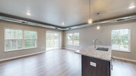 This well-appointed 2-bedroom, 2-bathroom unit at 801 Kraewood Dr in Northfield, MN offers a thoughtfully designed single-floor layout with modern finishes throughout. The open-concept kitchen and living area serves as the heart of the home, featuring a large granite island with an undermount sink, rich dark-toned cabinetry, stainless steel appliances, and pendant lighting. Exposed metallic ductwork adds an industrial accent to the living space, which is bathed in natural light through multiple large windows and a sliding glass door that opens to a private balcony overlooking greenery. Light-toned luxury vinyl plank flooring flows throughout the main living areas, complementing the neutral gray wall palette. The two bedrooms are carpeted for comfort, each featuring dedicated closets with built-in shelving. The primary bedroom is generously sized and includes its own walk-in closet. Both bathrooms are finished with granite-topped dark vanities and LVP flooring, with one featuring a full soaking tub and shower combo. Two hallways and additional closets provide ample storage. The unit also includes a dishwasher and in-unit access to well-organized utility spaces, making this a highly functional and stylish home.