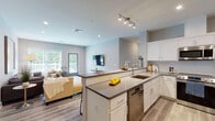Located at 11 Lafayette Dr in New Windsor, NY, this single-floor residence showcases a clean, contemporary design with light-toned walls, light wood-look flooring, and recessed lighting throughout. The open-concept kitchen and living area serves as the heart of the home, with the kitchen featuring white shaker cabinetry, quartz countertops, stainless steel appliances including a refrigerator, range, microwave, and dishwasher, and a central island with a built-in sink. The living area flows naturally from the kitchen, offering generous space for seating, a wall-mounted television, and direct access to a private outdoor deck through a glass-paneled door, inviting natural light and greenery views inside. The primary bedroom is well-proportioned, with large windows framing lush outdoor scenery and access to an expansive walk-in closet outfitted with wire shelving systems. The en-suite primary bathroom features marble-look tile flooring, a glass-enclosed walk-in shower with full-height tile surround, and a dark-toned vanity. A second bathroom offers a full tub-shower combination with subway-style tile. An additional room with a Murphy bed and garden views adds versatile functionality to this well-appointed residence.