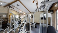 Located in Dublin, Ohio, this single-floor fitness center at 3970 Brelsford Lane offers a well-equipped workout facility designed to support a wide range of exercise routines. The space is characterized by its distinctive exposed wood beam ceiling accents, which lend a warm, rustic touch to the otherwise clean and functional interior. Recessed and track lighting illuminate the room effectively, ensuring a bright and energetic atmosphere throughout.

The facility is outfitted with an impressive array of strength training machines, including cable and weight-stack units suited for both upper and lower body workouts. Cardio equipment, including elliptical trainers, is also prominently featured, providing members with a comprehensive fitness experience without leaving the floor. The dark rubber flooring provides a durable, slip-resistant surface ideal for high-traffic exercise areas.

Large windows allow natural light to filter into the space, contributing to an open and inviting ambiance. Wall-mounted mirrors enhance the sense of space and allow users to monitor their form during workouts. Ceiling fans are positioned throughout to maintain airflow and comfort during exercise sessions. Overall, this fitness center combines practical amenities with a welcoming design to serve the needs of an active community.