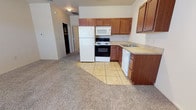 Located at 6302 Blake Ave in Amarillo, TX, this single-floor unit offers a practical and functional layout designed for comfortable everyday living. The kitchen is outfitted with warm-toned wood cabinetry providing ample storage, light-colored countertops, and a full suite of white appliances including a refrigerator, electric range with oven, built-in microwave, and dishwasher. The kitchen floor features neutral ceramic tile that transitions seamlessly into the open living area, which is finished with wall-to-wall carpet for a cozy feel. A ceiling fan with light fixture overhead and a window allowing natural light enhance the living space. The layout includes an entry area with direct access to the exterior, providing convenient ingress and egress. A dedicated bedroom features plush carpet flooring and clean neutral walls, offering a quiet and versatile space. The bathroom is finished with tile flooring and includes a full tub-shower combination. Throughout the unit, the neutral color palette of cream and beige tones creates a clean, move-in-ready environment. The open flow between the kitchen and living areas gives the space an airy, connected feel well-suited for a variety of living arrangements.